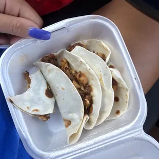 a person holding a plastic container filled with tacos