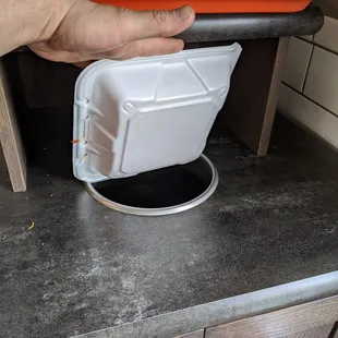 a hand holding a plastic container over a hole