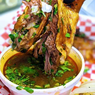 a hand holding a piece of meat over a bowl of soup