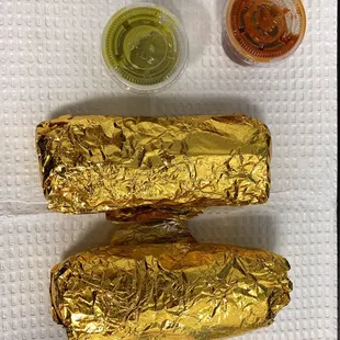 two burritos wrapped in gold foil