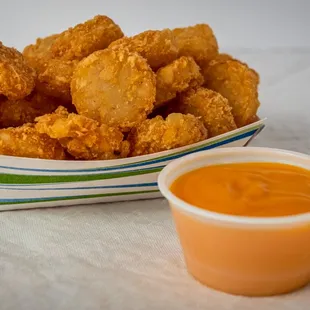 a basket of fried chicken nuggies next to a cup of sauce