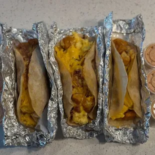 One potato, bacon, egg, and cheese in the middle and two  potato bean and cheese breakfast tacos with chipotle sauce on the side.