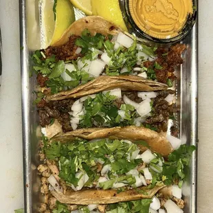 a tray of tacos and a side of sauce