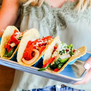 a woman holding a tray of tacos