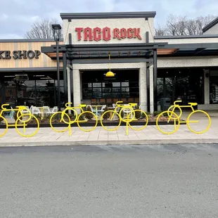 a row of yellow bicycles parked in front of a taco shop