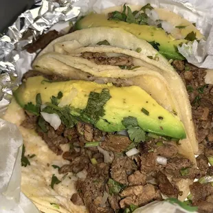 Beef Fajita Tacos with white cheese, onion, cilantro, avocado, green salsa, and lime.