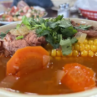 a bowl of soup with corn, carrots, and meat