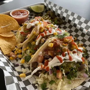 Steak tacos with lettuce, pico, cilantro, red onion, hot salsa, green salsa, corn, sriracha, and a lime wedge.