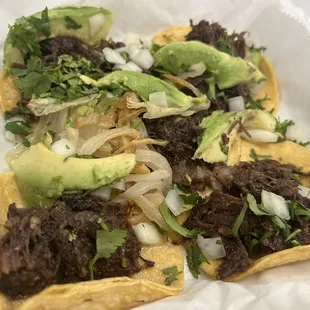 Barbacoa street tacos with avocado and grilled onions on the side.