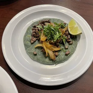 One taco asado with grilled onions, cilantro, and a wedge of lime.