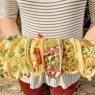 a woman holding four tacoss