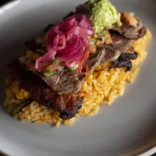 Platano Relleno: Tender steak over fried plantains, melted cheese, pico de gallo, pickled onions, guacamole, and rice for a bold twist.