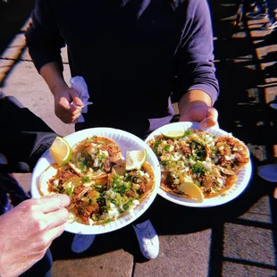 a man holding two plates of tacos
