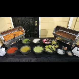 Condiments table with rice and beans (cilantro,onions,radishes,limes,deviled cucumbers, guacamole red and green salsa)