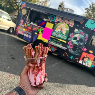 a person holding a cup of food in front of a food truck