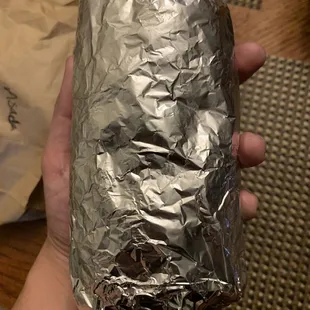a hand holding a foil wrapped burrito