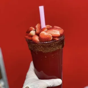 a hand holding a tall glass with strawberries in it
