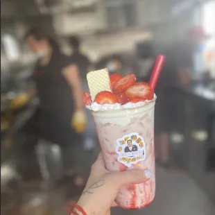 a hand holding a strawberry milkshake