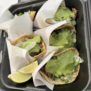 three tacoss with guacamole and lime wedges