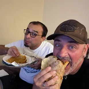 two men sitting on a couch eating