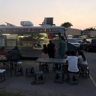 a group of people sitting at tables in a parking lot