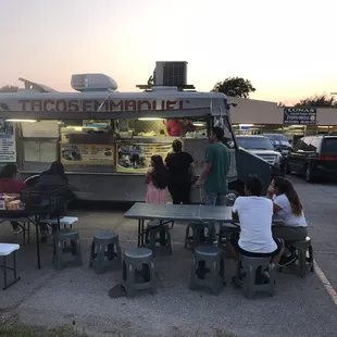 a group of people sitting at tables in a parking lot