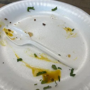 a white paper plate with a spoon and sauce on it