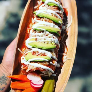 a hand holding a wooden plate with a long taco