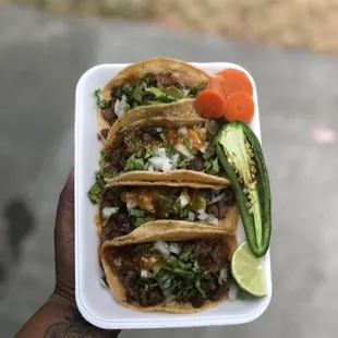a hand holding a plate of tacos