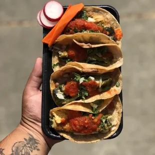 a hand holding a tray of tacos
