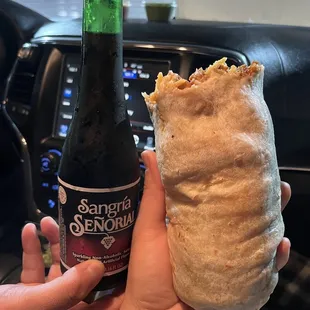 a person holding a bottle of beer and a burrito