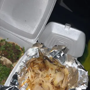 a takeout container with onions and meat