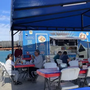 people sitting at tables under a blue tent