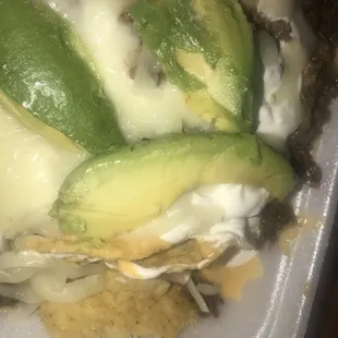 a close up of a taco topped with cheese and avocado