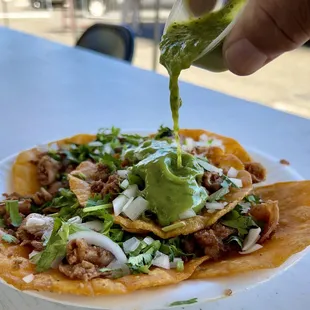 a hand drizzing guacamole over a tortilla
