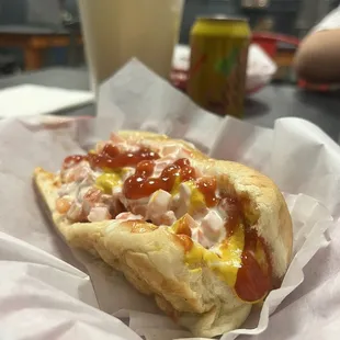 Plain hotdog with mayo, mustard, ketchup, tomato and grilled onions; with the weenie wrapped in bacon.