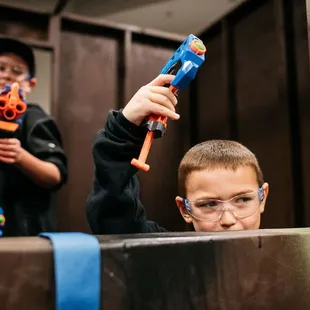 Concentration is key! Young players peek over barriers, blasters ready for the next tag at Tactical Urban Combat.