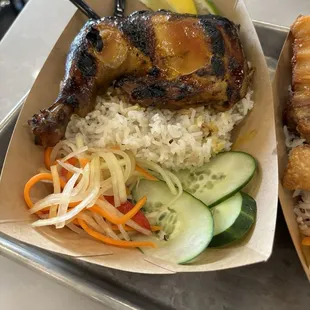 Chicken inasal over a bed of garlic rice , a side of sliced cucumber and pickled vegetables carrots and papaya, referred to as attchara.