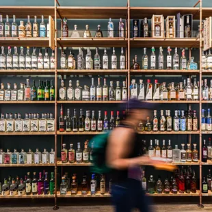 a woman walking past a wall of liquor bottles