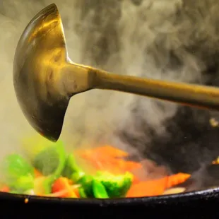 a person stirring vegetables in a wok