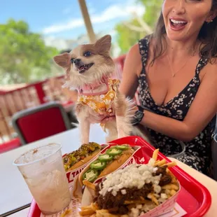  a woman sitting at a table with a tray of food and a dog