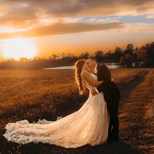 a bride and groom kissing in a field at sunset