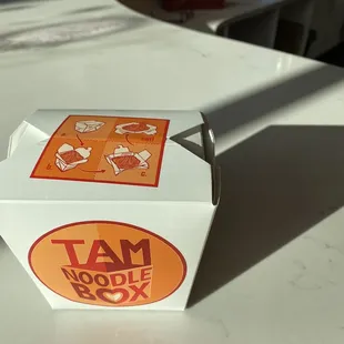 a tam noodle box on a table