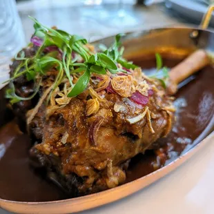 Dum Ki Nalli Gosht. $47. Slow-cooked 10 hours, lamb shank roasted in aromatic gravy with saffron rice and burani raita.