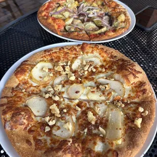 Individual sized pizza one with goat cheese and pear and another with veggies