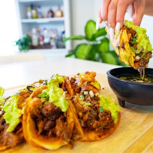 a person dipping sauce onto a plate of tacos