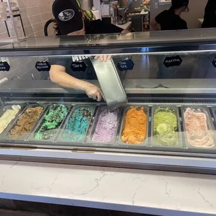 a person scooping ice cream into a display case