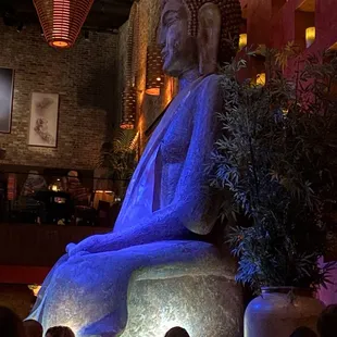 Giant Buddha statue, sitting in front of a tall wall of lanterns
