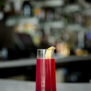a red drink with a slice of lemon on the rim