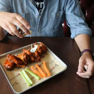a person sitting at a table with a tray of wings and carrots